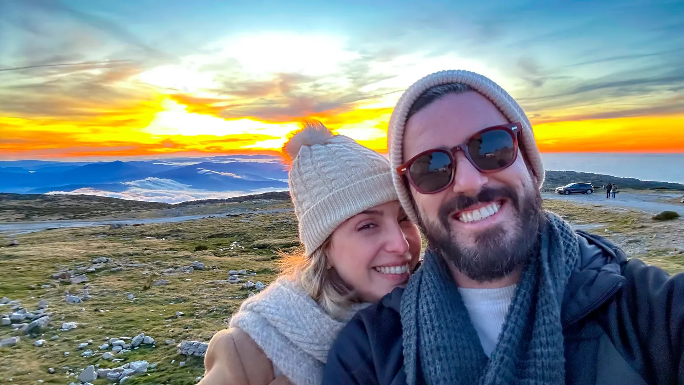 O casal em uma selfie com o pôr do sol na serra ao fundo