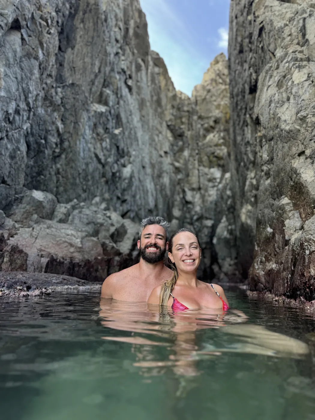 O casal dentro da água, cercado por grandes pedras
