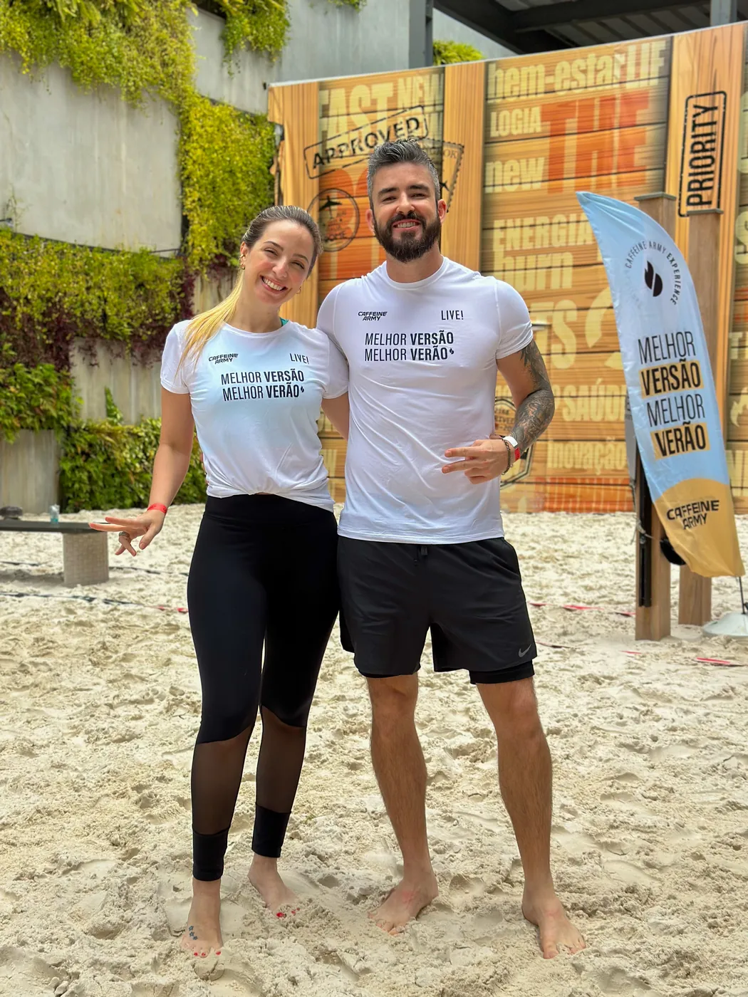 O casal lado a lado em um evento de praia, fazendo sinal de paz