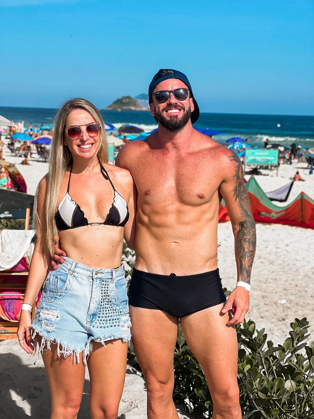 O casal na praia, com o mar e os morros do Rio ao fundo