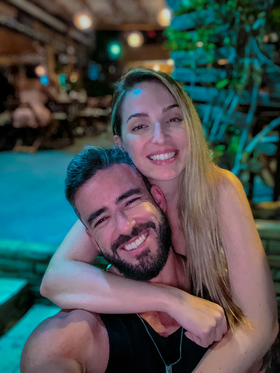 Agnes abraçada a Thiago, os dois sorrindo, em uma noite quente